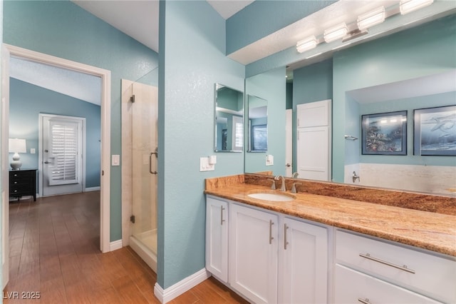 full bath featuring a stall shower, vanity, baseboards, and wood finished floors