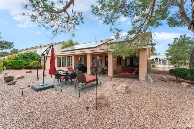 rear view of property with stucco siding, a patio, roof mounted solar panels, and fence