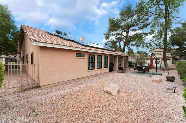 back of property with a patio, a fenced backyard, stucco siding, a tile roof, and roof mounted solar panels