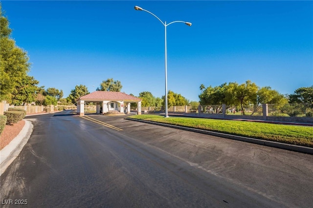 view of road featuring curbs, street lighting, and a gated entry