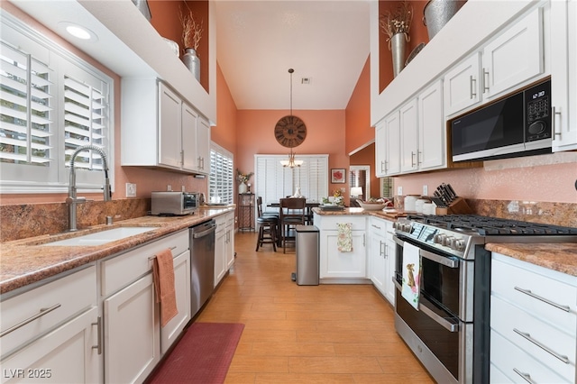 kitchen with light wood finished floors, appliances with stainless steel finishes, white cabinetry, and a sink