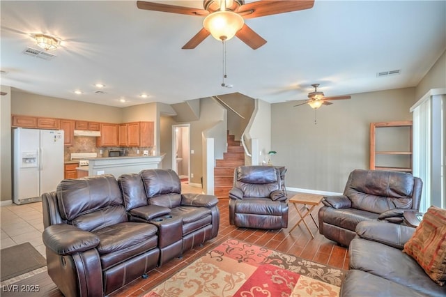 living room with visible vents, baseboards, ceiling fan, and stairway