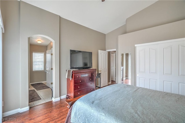 bedroom with wood finished floors, baseboards, high vaulted ceiling, arched walkways, and a closet