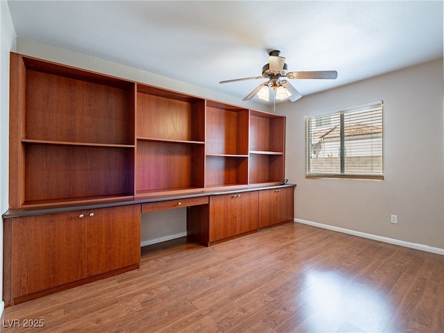 unfurnished office featuring baseboards, a ceiling fan, wood finished floors, and built in desk