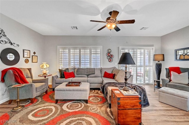 living room featuring ceiling fan, visible vents, baseboards, and wood finished floors