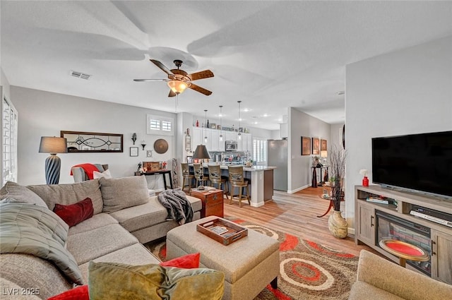 living area with a ceiling fan, visible vents, light wood finished floors, and baseboards