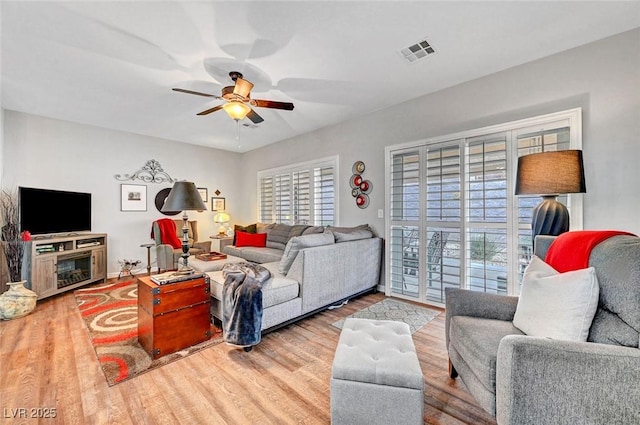 living room with baseboards, wood finished floors, visible vents, and ceiling fan