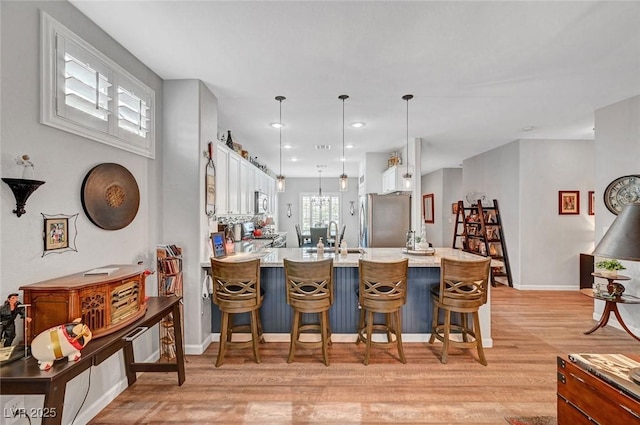 kitchen featuring light wood-style flooring, white cabinets, stainless steel appliances, and a kitchen breakfast bar