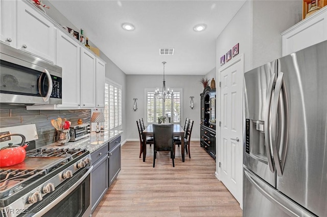 kitchen featuring tasteful backsplash, light wood-type flooring, an inviting chandelier, white cabinets, and stainless steel appliances