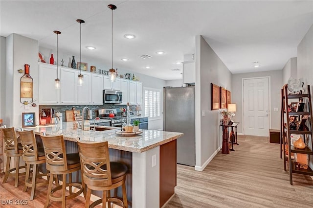 kitchen featuring visible vents, light stone countertops, decorative backsplash, appliances with stainless steel finishes, and a peninsula