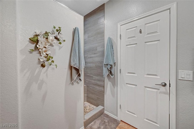 full bathroom featuring tile patterned floors, a textured wall, and a tile shower