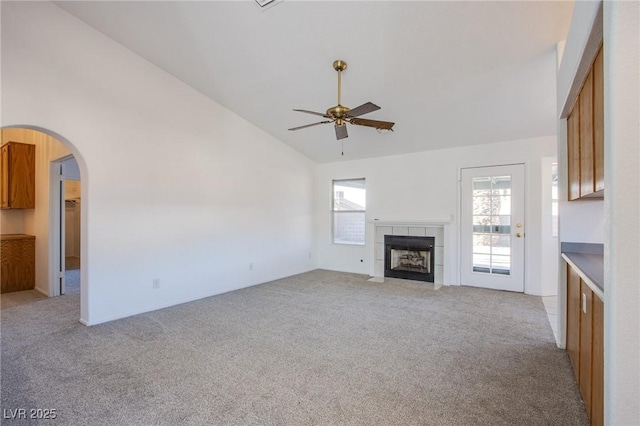 unfurnished living room with high vaulted ceiling, arched walkways, light colored carpet, ceiling fan, and a tile fireplace