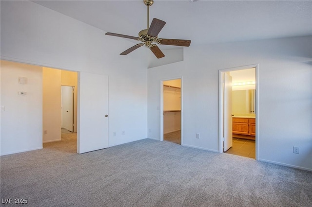 unfurnished bedroom featuring a spacious closet, connected bathroom, light carpet, high vaulted ceiling, and a ceiling fan