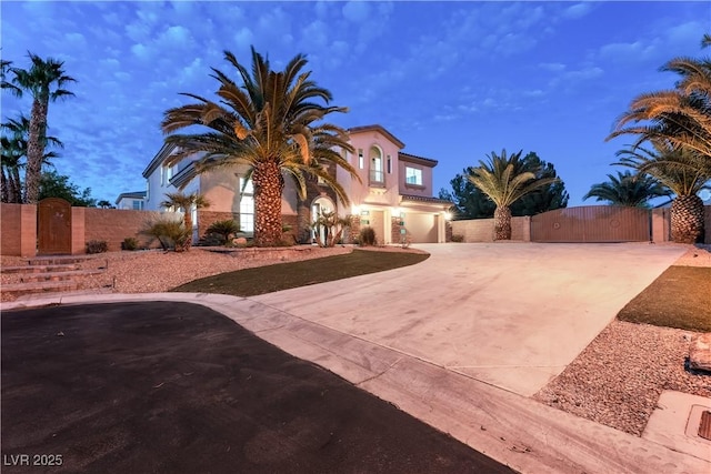 mediterranean / spanish house with stucco siding, driveway, an attached garage, and a gate