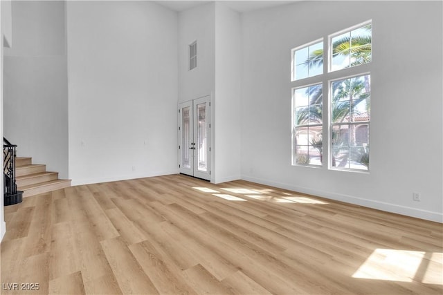 unfurnished living room with baseboards, stairway, light wood-type flooring, french doors, and a towering ceiling