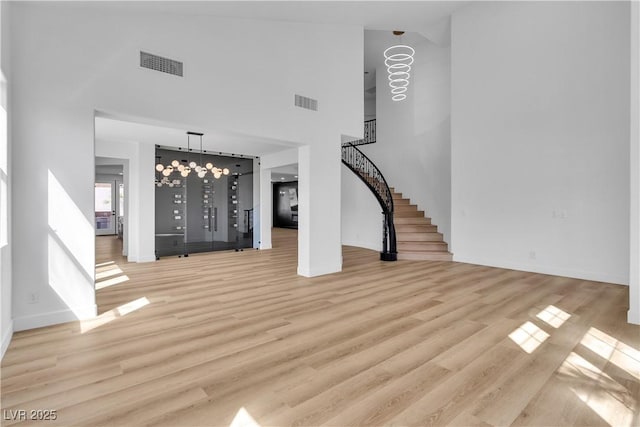 interior space featuring light wood-type flooring, visible vents, a towering ceiling, and stairway