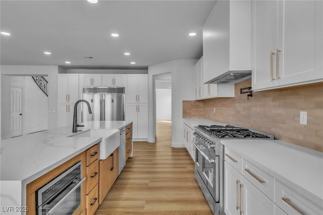 kitchen featuring white cabinets, high end appliances, custom range hood, and a sink