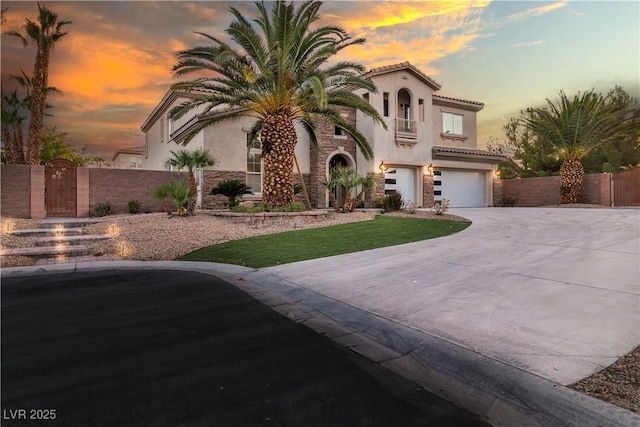 mediterranean / spanish-style home featuring a gate, stone siding, an attached garage, and stucco siding