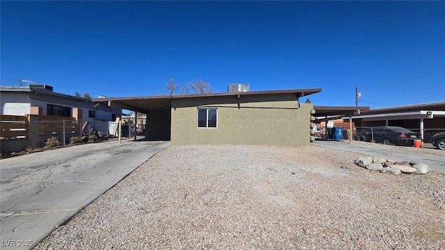 rear view of property featuring fence, driveway, central AC, stucco siding, and a carport