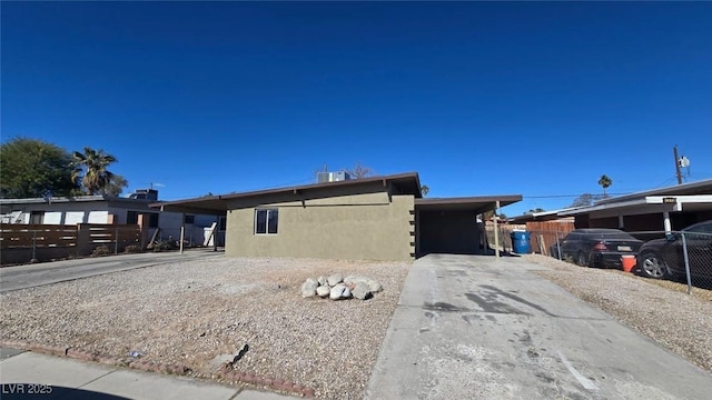 view of front of house featuring stucco siding, an attached carport, driveway, and fence