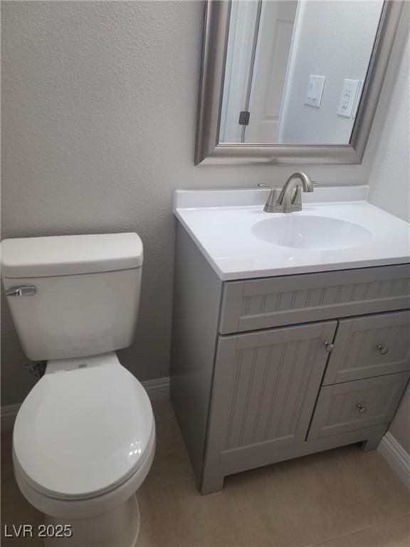 half bath with baseboards, toilet, vanity, and tile patterned flooring