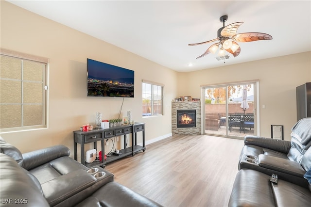 living area with a ceiling fan, visible vents, baseboards, a fireplace, and light wood-style floors