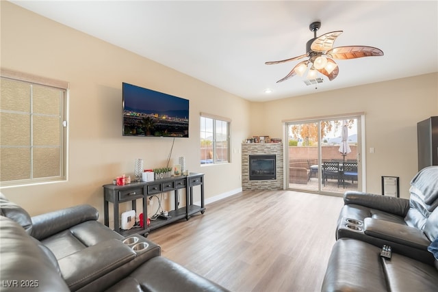 living room featuring baseboards, visible vents, a fireplace, ceiling fan, and light wood-type flooring