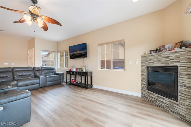 living room with a glass covered fireplace, a ceiling fan, baseboards, and wood finished floors