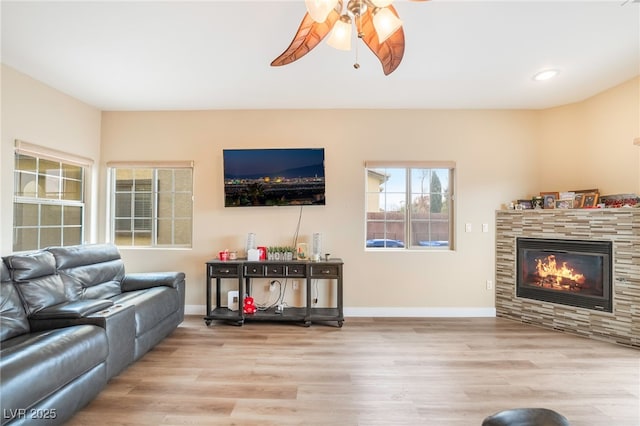 living area featuring a glass covered fireplace, wood finished floors, recessed lighting, baseboards, and ceiling fan