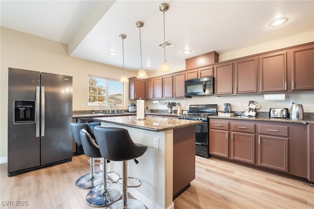 kitchen with a center island, dark stone countertops, a kitchen breakfast bar, black appliances, and a sink