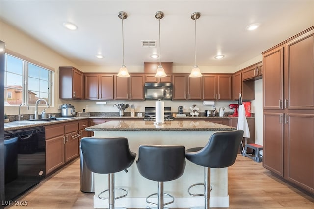 kitchen with a sink, black appliances, light wood-style flooring, and a center island