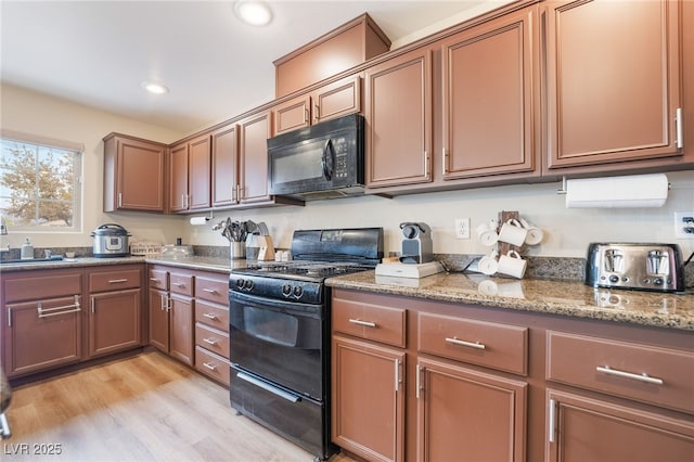 kitchen featuring light stone counters, light wood finished floors, recessed lighting, a sink, and black appliances