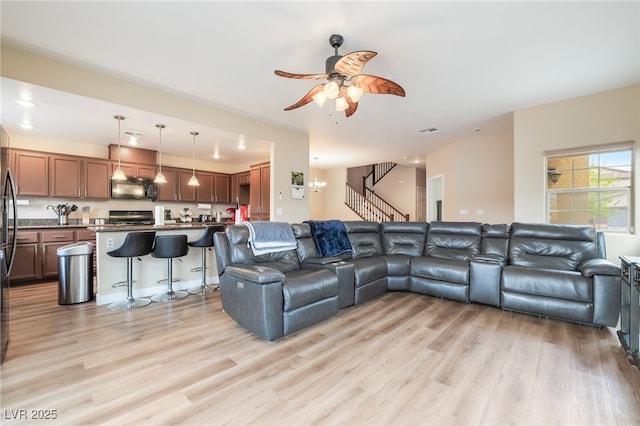 living room featuring light wood finished floors, visible vents, ceiling fan with notable chandelier, and stairs