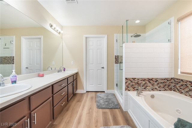 full bath with a sink, wood finished floors, a jetted tub, and a stall shower