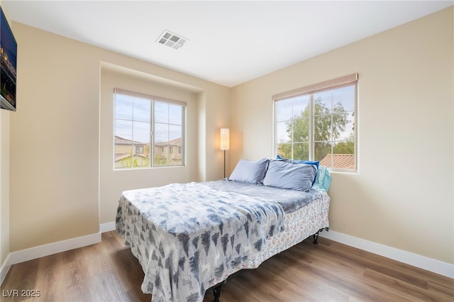 bedroom with visible vents, multiple windows, baseboards, and wood finished floors