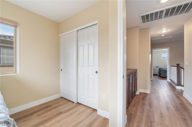 hall with light wood-style flooring, an upstairs landing, baseboards, and visible vents