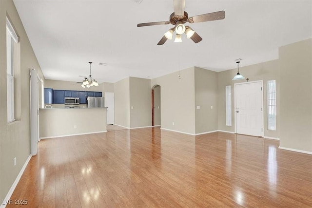 unfurnished living room with baseboards, arched walkways, light wood-style flooring, and ceiling fan with notable chandelier