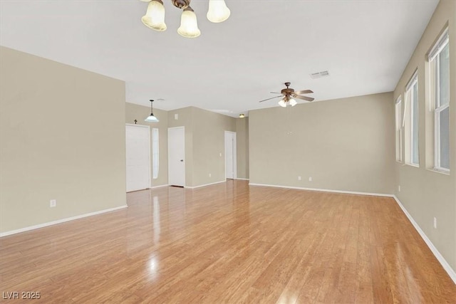 unfurnished room with ceiling fan with notable chandelier, light wood-style flooring, baseboards, and visible vents