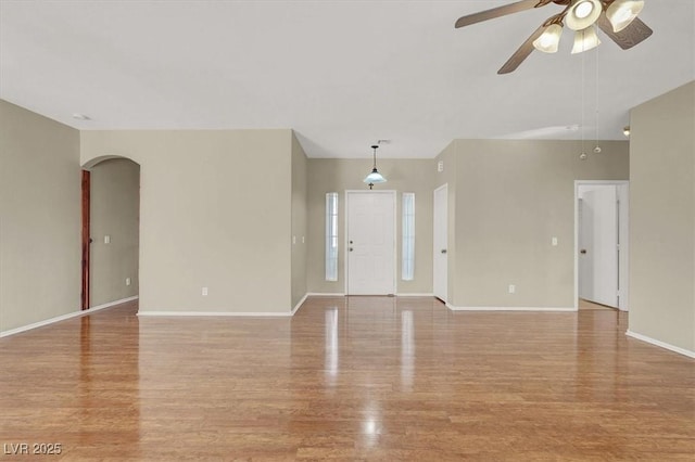 unfurnished living room with arched walkways, baseboards, light wood-style floors, and a ceiling fan