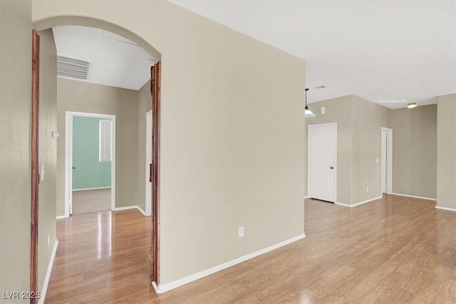 spare room with arched walkways, visible vents, light wood-type flooring, and baseboards