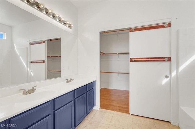 bathroom featuring double vanity, a sink, a spacious closet, tile patterned floors, and a washtub