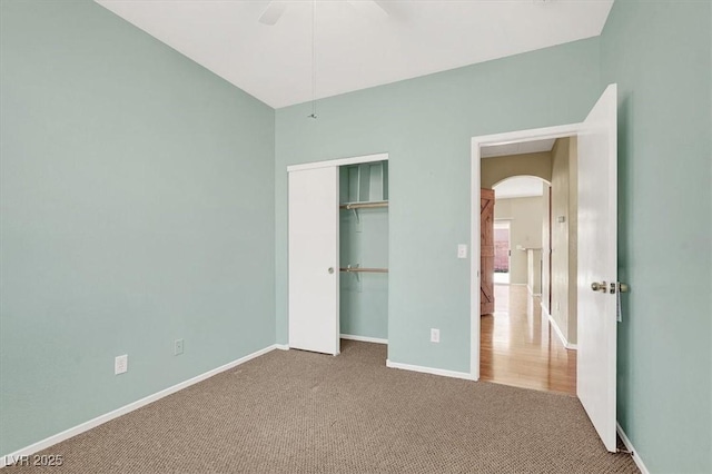 unfurnished bedroom featuring a ceiling fan, baseboards, carpet floors, arched walkways, and a closet