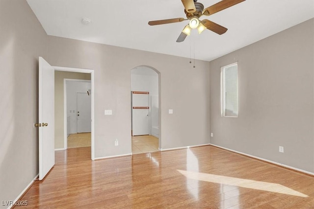 unfurnished bedroom featuring a walk in closet, baseboards, light wood-style floors, arched walkways, and a ceiling fan