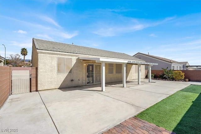 rear view of property featuring a patio, a gate, fence, and stucco siding