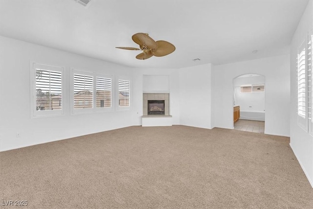 unfurnished living room featuring a fireplace, carpet, arched walkways, and ceiling fan