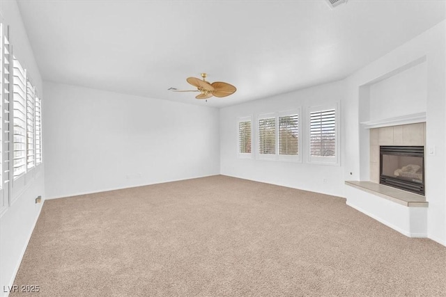 unfurnished living room with a tiled fireplace, ceiling fan, and carpet floors