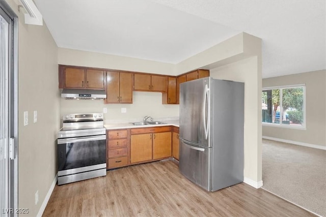 kitchen with baseboards, under cabinet range hood, light countertops, appliances with stainless steel finishes, and a sink