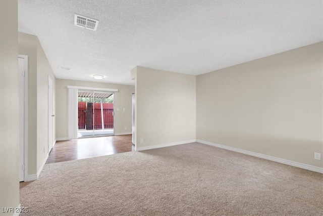 spare room with visible vents, light carpet, a textured ceiling, and baseboards