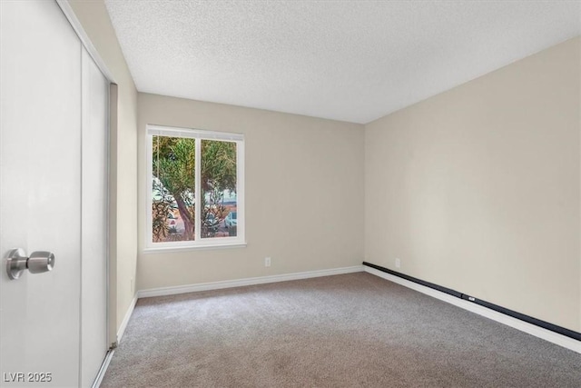 empty room with baseboard heating, a textured ceiling, baseboards, and carpet floors