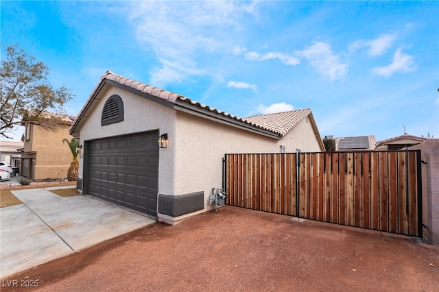 garage featuring concrete driveway, fence, and a gate